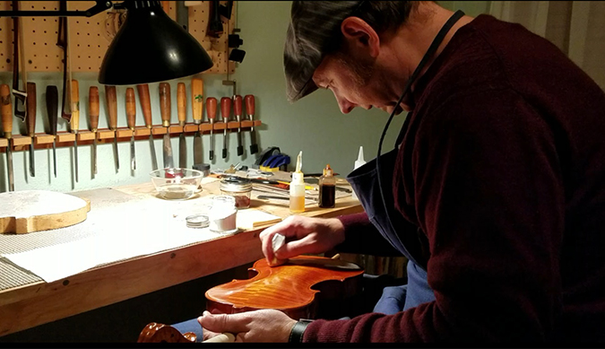 Tumbas works on a violin in his workshop. Tumbas works on a violin in his workshop.