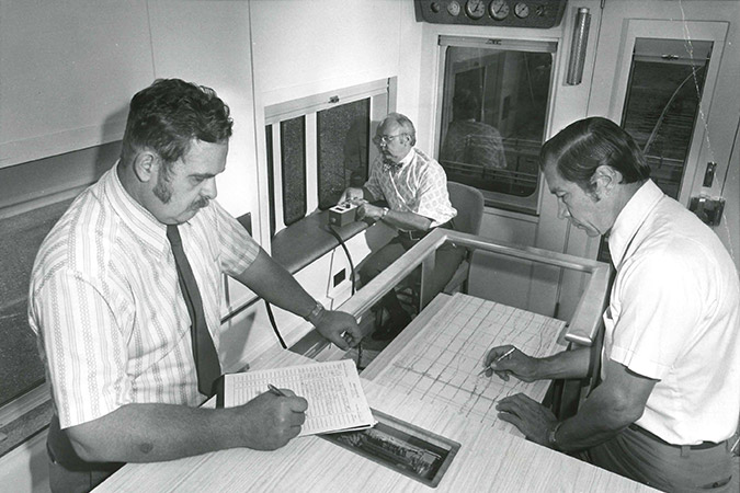 Atchison, Topeka and Santa Fe employees manually review track geometry strip charts on the geo cars in the 1970s. Atchison, Topeka and Santa Fe employees manually review track geometry strip charts on the geo cars in the 1970s.