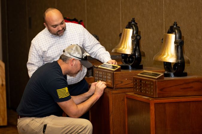Heartland Division General Manager Tony Fulton watches as Aaron Stich, electrician, applies a nameplate to one of their bells.  Heartland Division General Manager Tony Fulton watches as Aaron Stich, electrician, applies a nameplate to one of their bells.