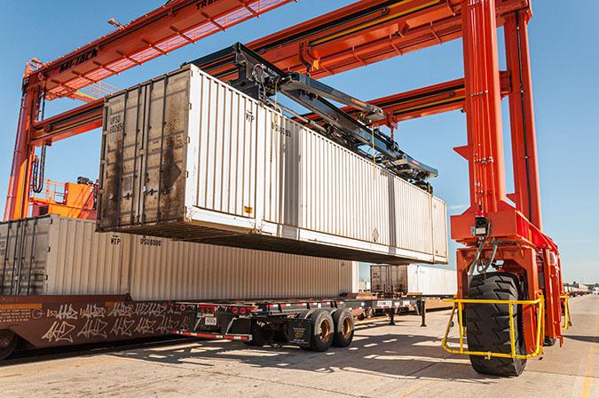 An overhead rubber tire crane moves a trailer in position. An overhead rubber tire crane moves a trailer in position.